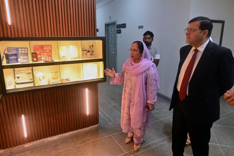 A faculty member briefing the Director at a lit display cabinet of IRCBM products